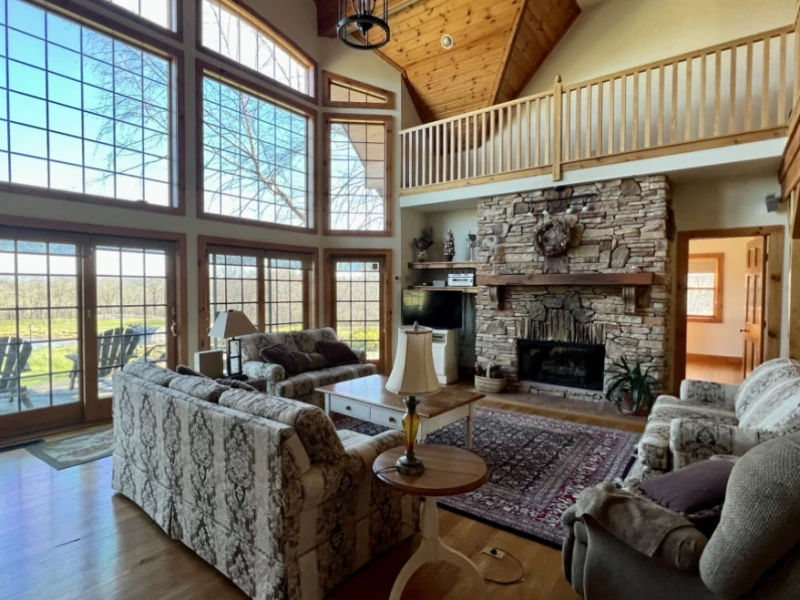 living room of farm house with stone fireplace and view out the two story front windows